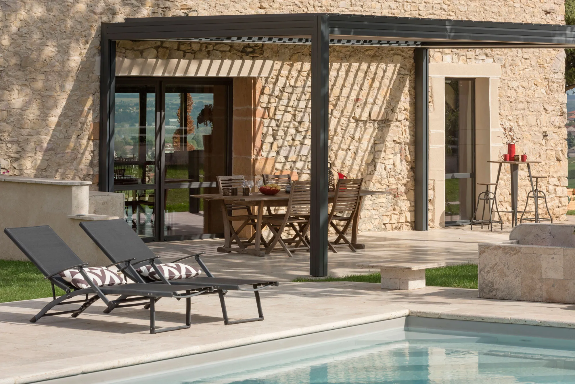 Pergola bioclimatique sur une terrasse en pierre avec piscine, dans le Lyonnais